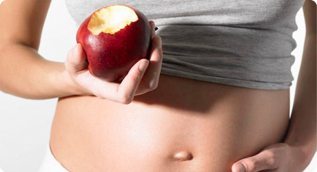 Femme enceinte présentant une pomme croquée.